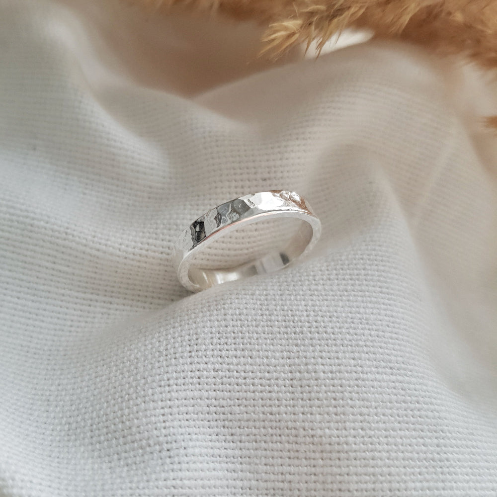 a 3mm wide silver ring with a hammered finish on white fabric background
