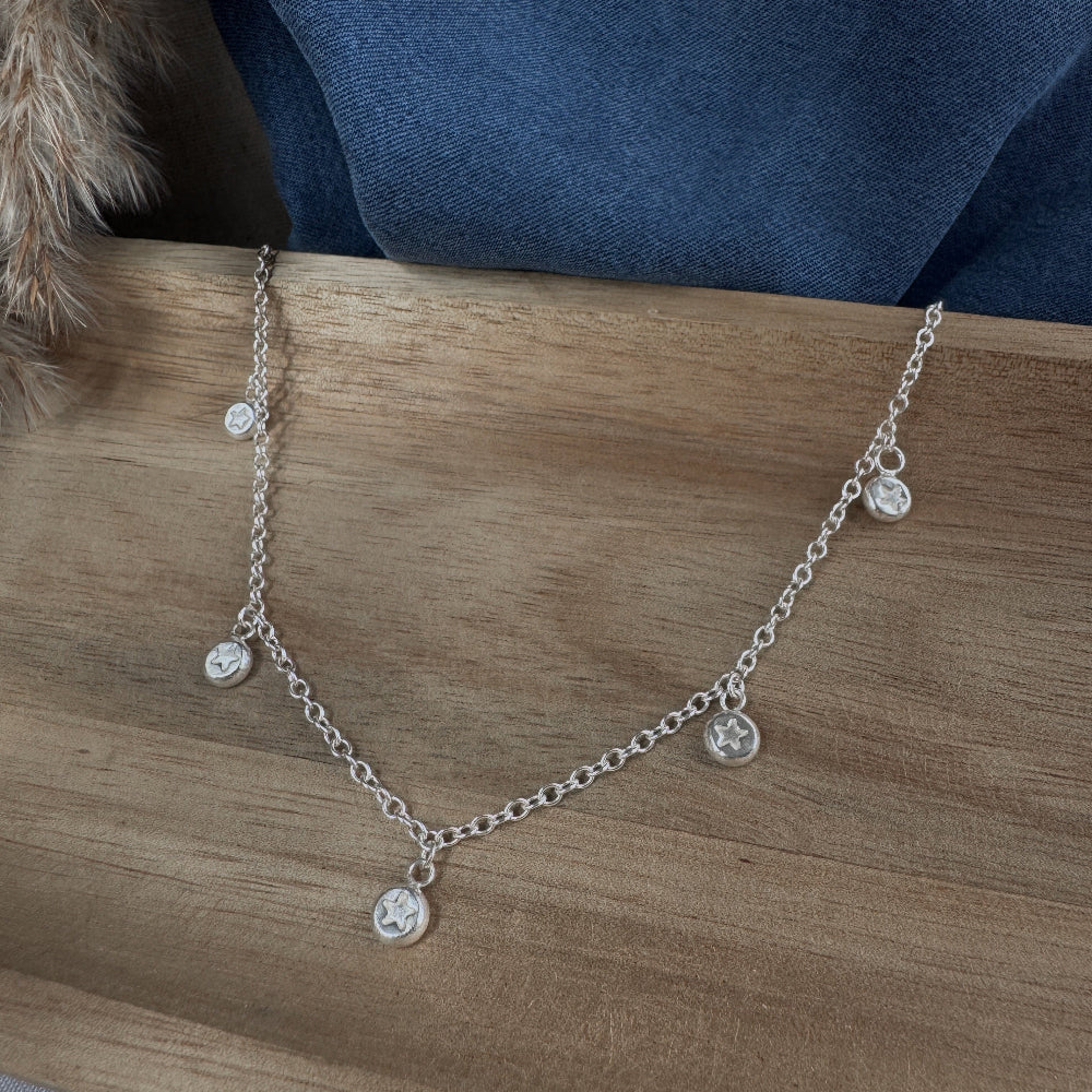 Silver necklace with small round star charms on a wooden surface