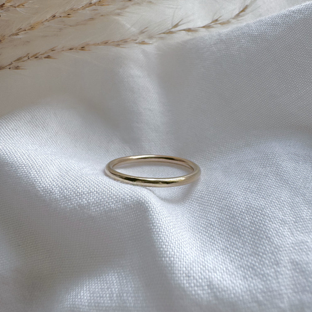 a simple gold plain band ring on a white fabric background