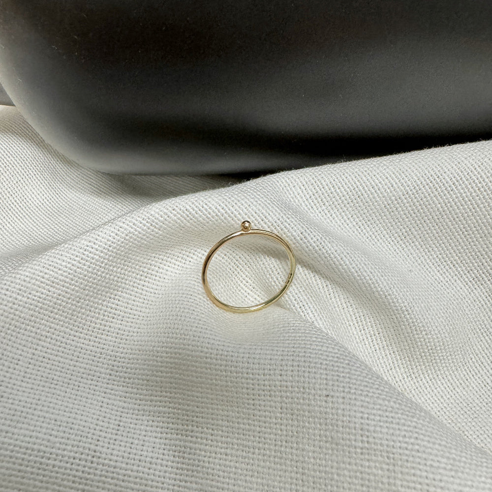 A 9ct gold ball stacking ring with a small ball on top, placed on a white textured surface.