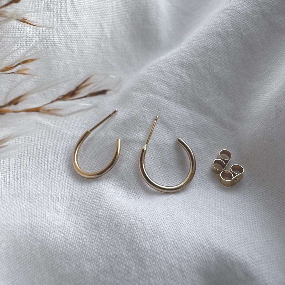 A pair of 9ct gold hoop earrings placed on a white fabric surface.
