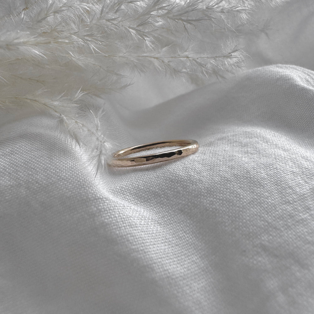 A hammered 9ct gold infinity ring placed on a white fabric with a feather-like texture in the background.
