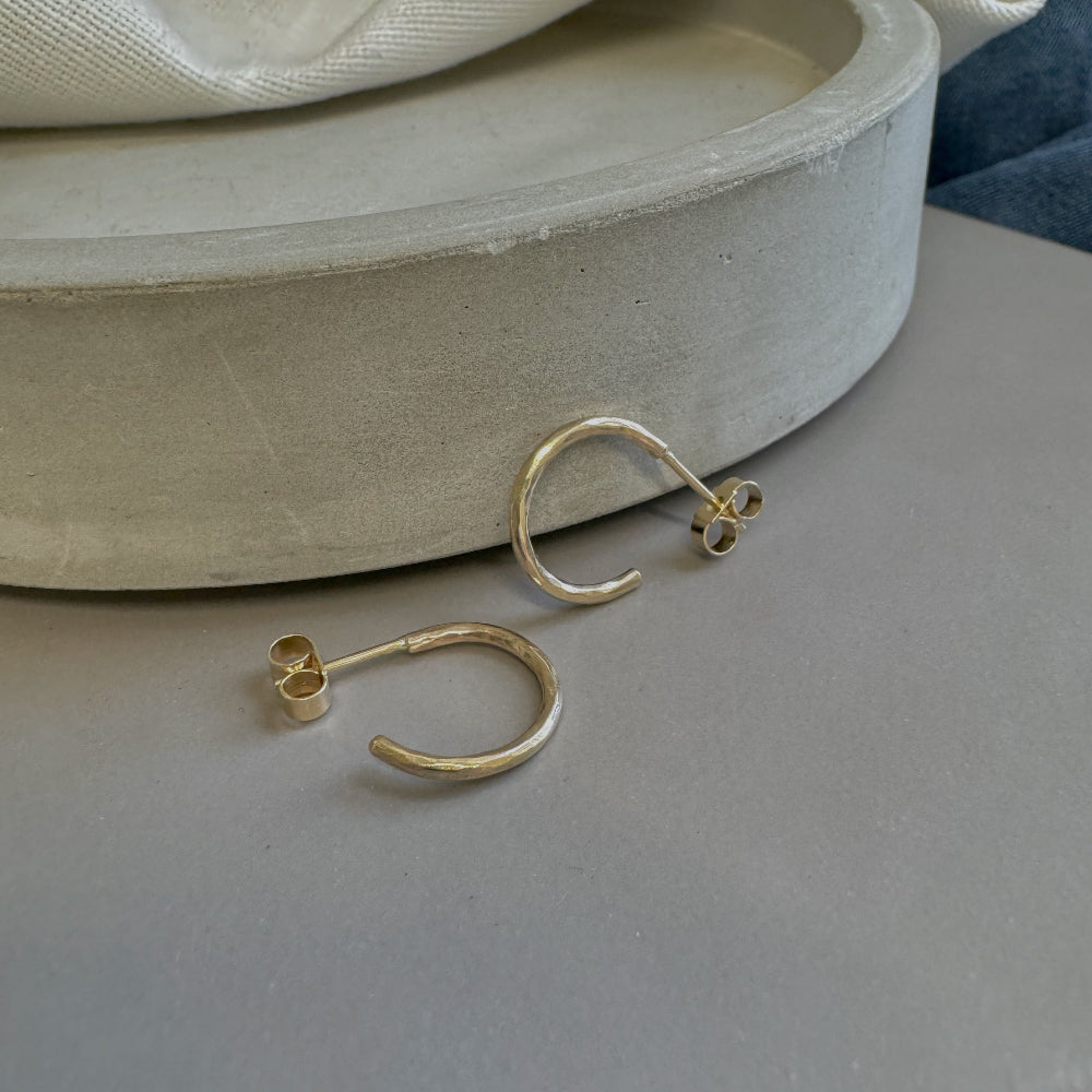 A pair of small hammered 9ct gold hoop earrings placed on a grey surface in front on a dish