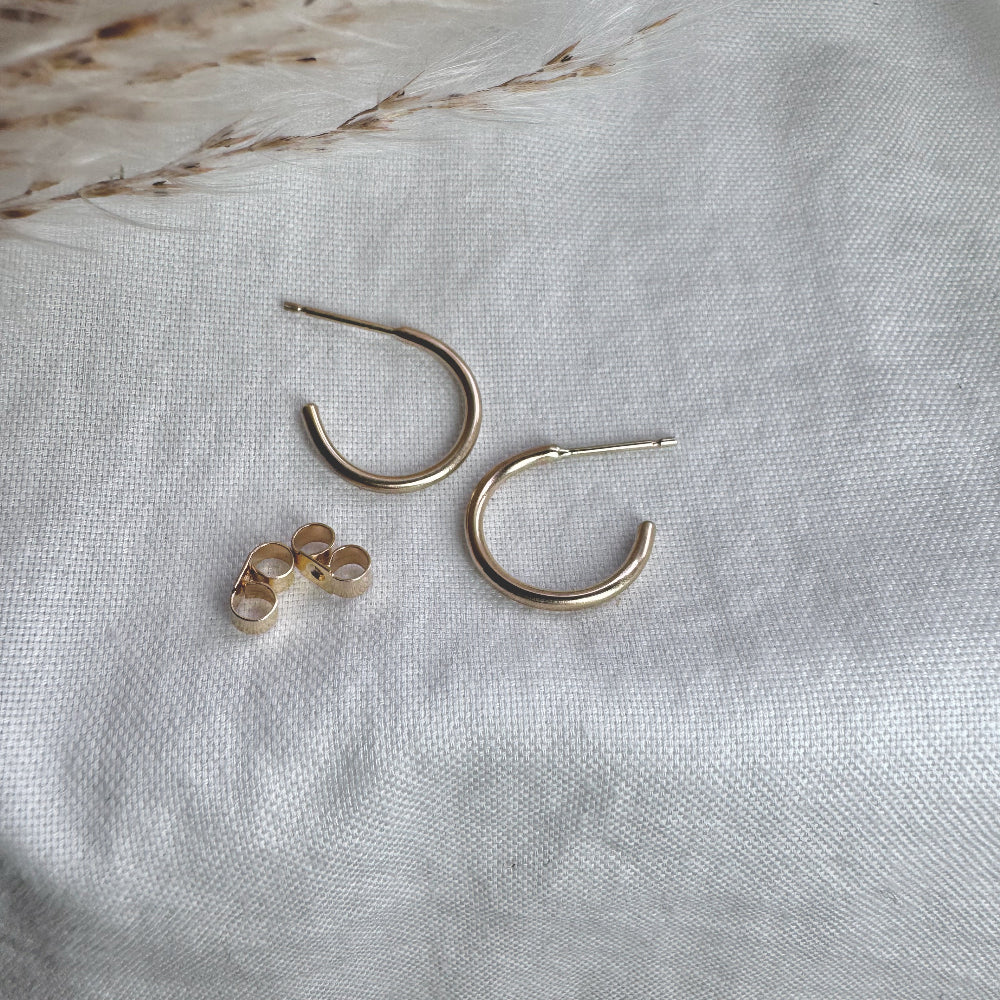 A pair of 9ct gold hoop earrings placed on a white fabric surface.