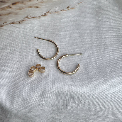 A pair of 9ct gold hoop earrings placed on a white fabric surface.
