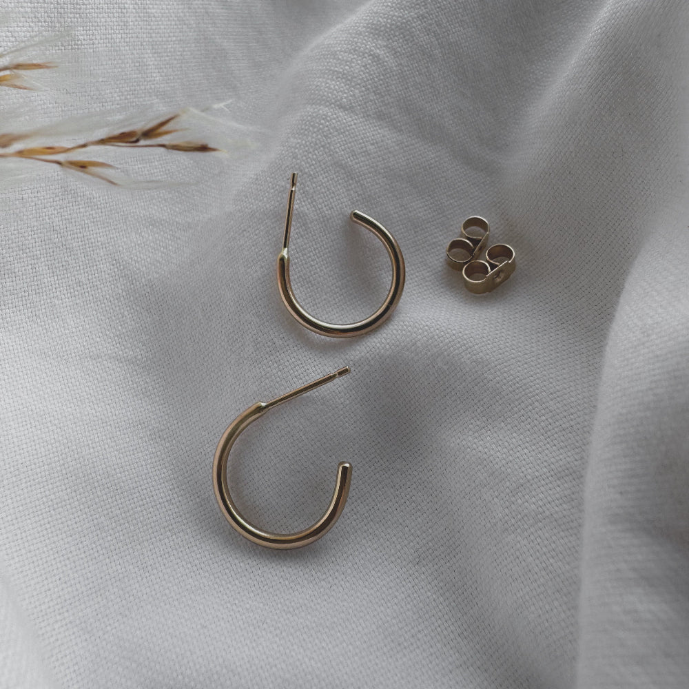 A pair of 9ct gold hoop earrings placed on a white fabric surface.