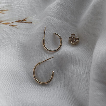 A pair of 9ct gold hoop earrings placed on a white fabric surface.