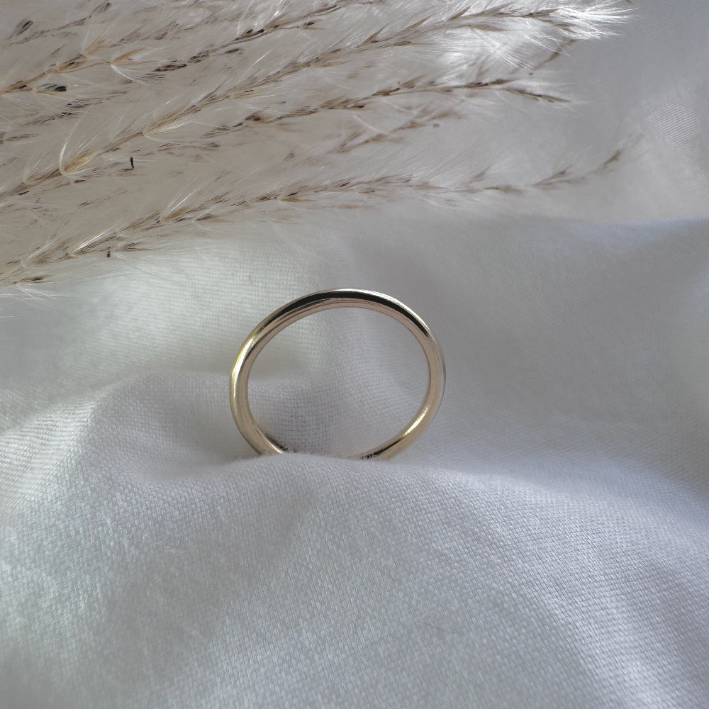 a simple gold plain band ring on a white fabric background