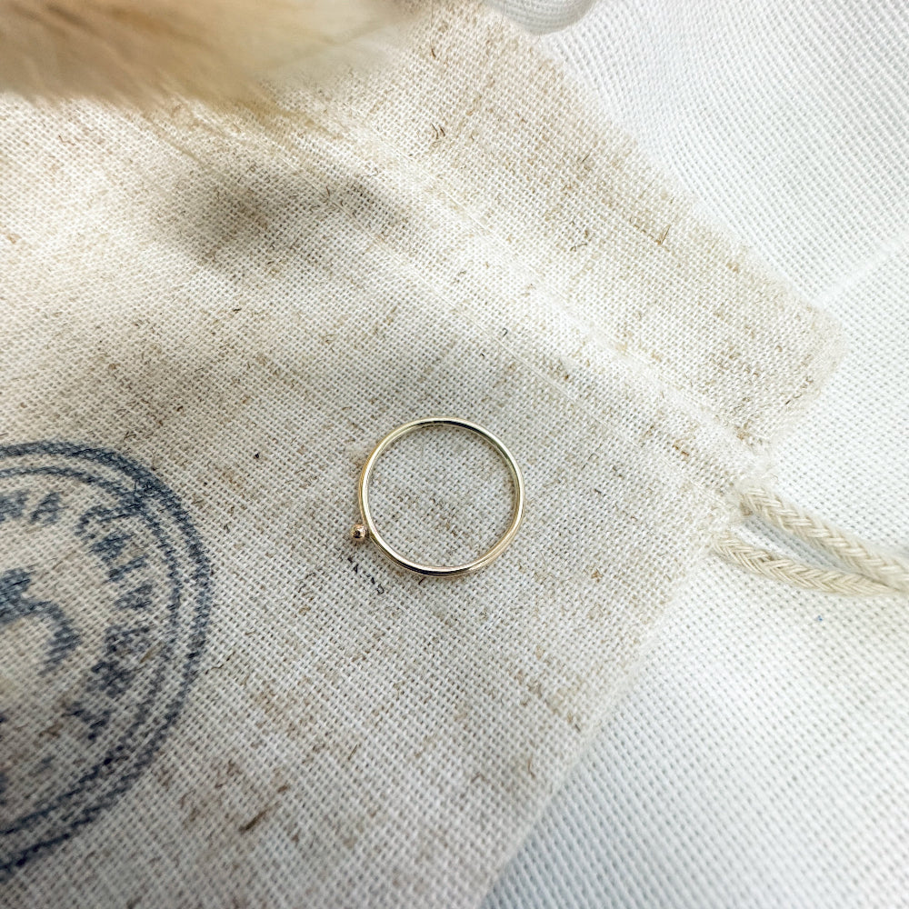A 9ct gold ball stacking ring with a small ball on top, placed on a white textured surface.