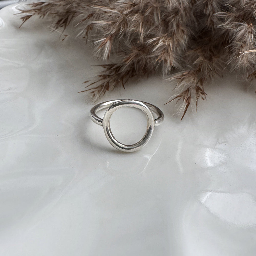 Silver circle ring on a white surface with dried plants in the background