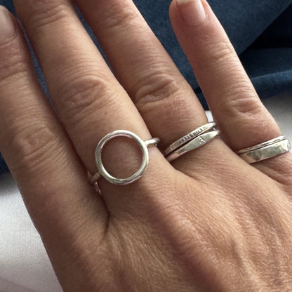 Hand wearing two silver rings on a neutral background