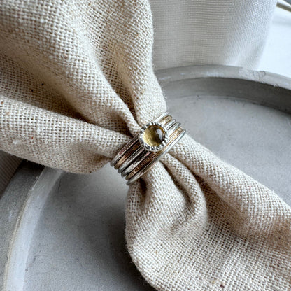 5mm citrine set in a rustic setting on a thin silver band mixed with a thin gold band each side and then a thin silver band either side of that. Shown as a set on a piece of fabric