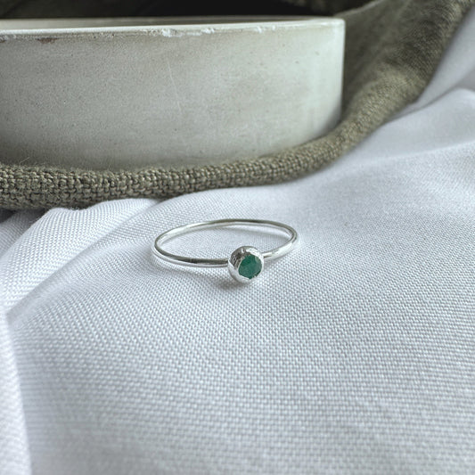 A dainty emerald and silver ring with a 3mm stone, placed on a white fabric surface.