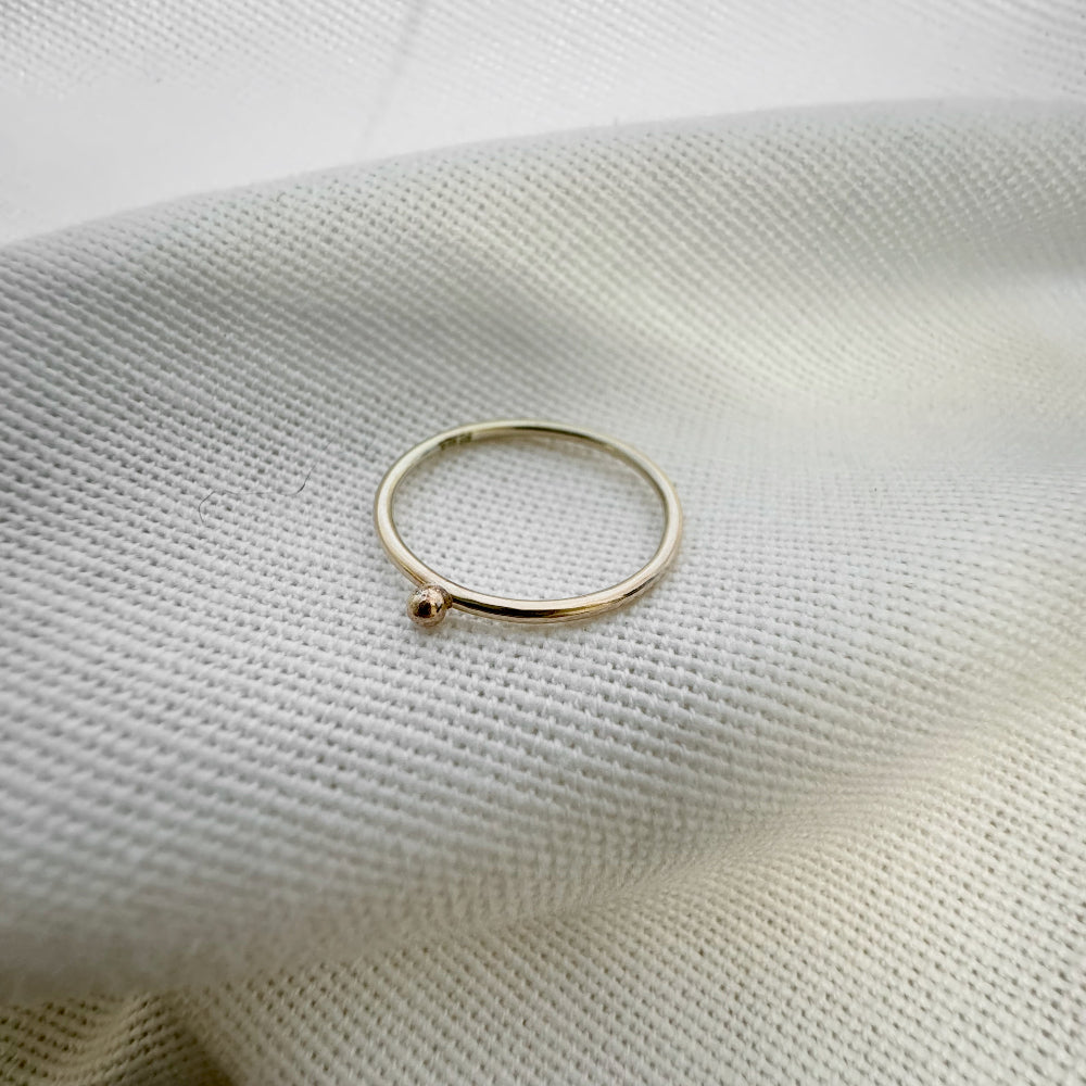 A 9ct gold ball stacking ring with a small ball on top, placed on a white textured surface.