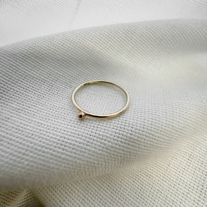 A 9ct gold ball stacking ring with a small ball on top, placed on a white textured surface.