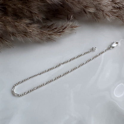 Dainty Silver figaro chain bracelet on a white surface with dried gresses in the background