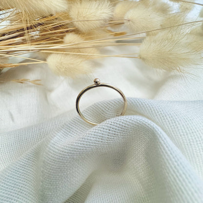 A 9ct gold ball stacking ring with a small ball on top, placed on a white textured surface with dried grasses in the background