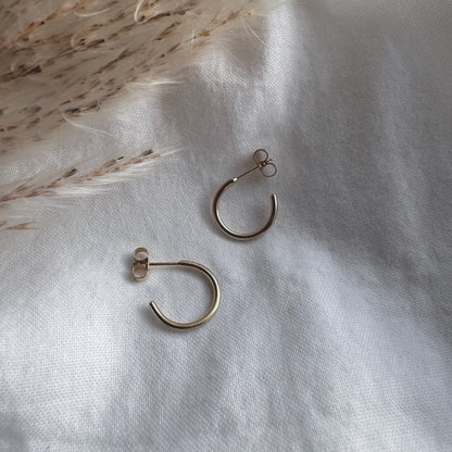 A pair of 9ct gold hoop earrings placed on a white fabric surface.