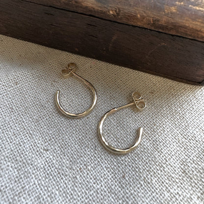A pair of small hammered 9ct gold hoop earrings placed on a textured fabric surface 