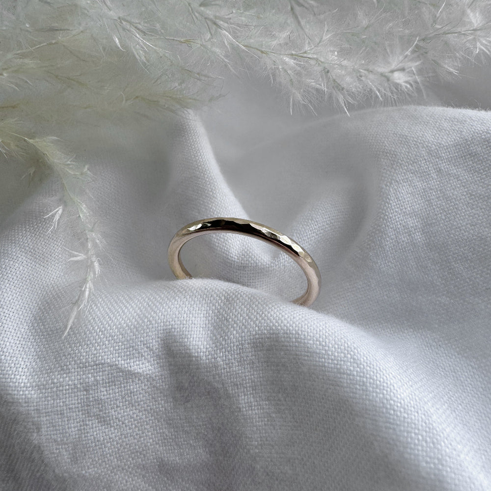 A hammered 9ct gold infinity ring placed on a white fabric with a feather-like texture in the background.