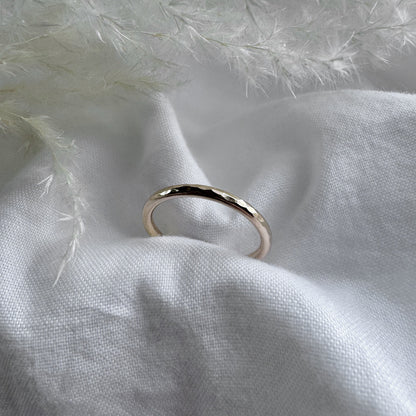 A hammered 9ct gold infinity ring placed on a white fabric with a feather-like texture in the background.