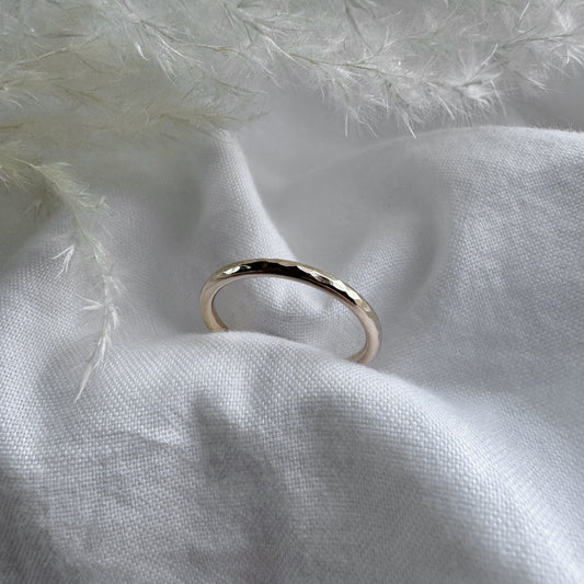 A hammered 9ct gold infinity ring placed on a white fabric with a feather-like texture in the background.