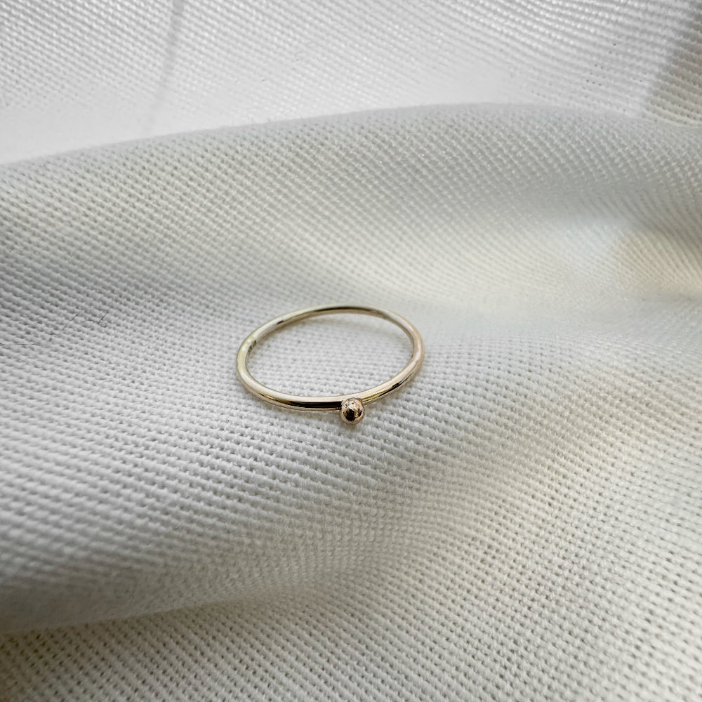 A 9ct gold ball stacking ring with a small ball on top, placed on a white textured surface.