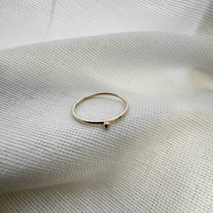 A 9ct gold ball stacking ring with a small ball on top, placed on a white textured surface.