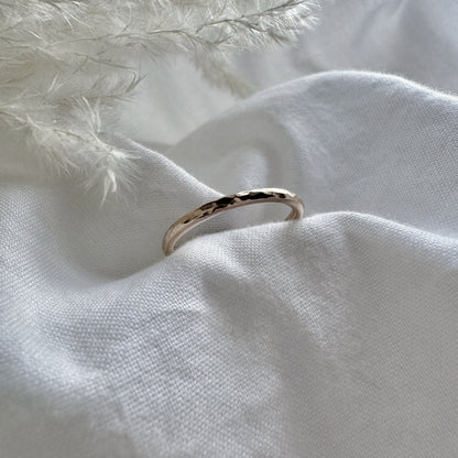 A hammered 9ct gold infinity ring placed on a white fabric with a feather-like texture in the background.