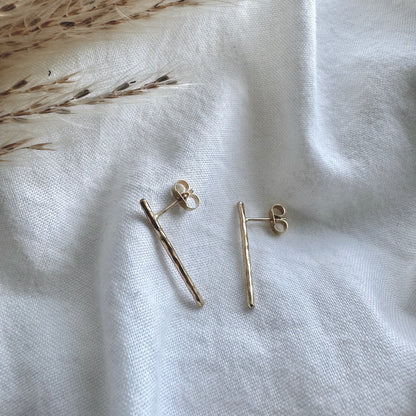A pair of hammered gold bar earrings placed on a white fabric surface.