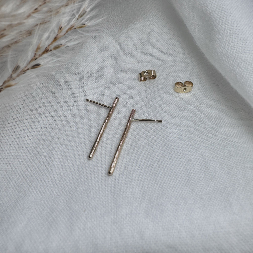 A pair of hammered gold bar earrings placed on a white fabric surface.