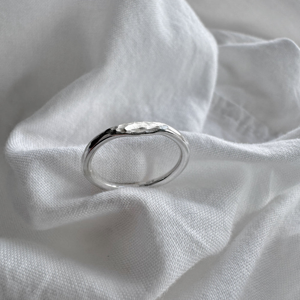 A silver hammered signet ring resting on a crumpled white fabric surface.