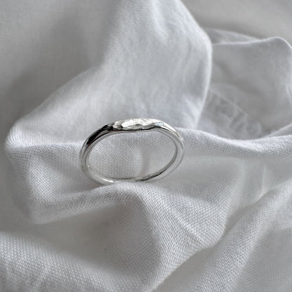 A silver hammered signet ring resting on a crumpled white fabric surface.