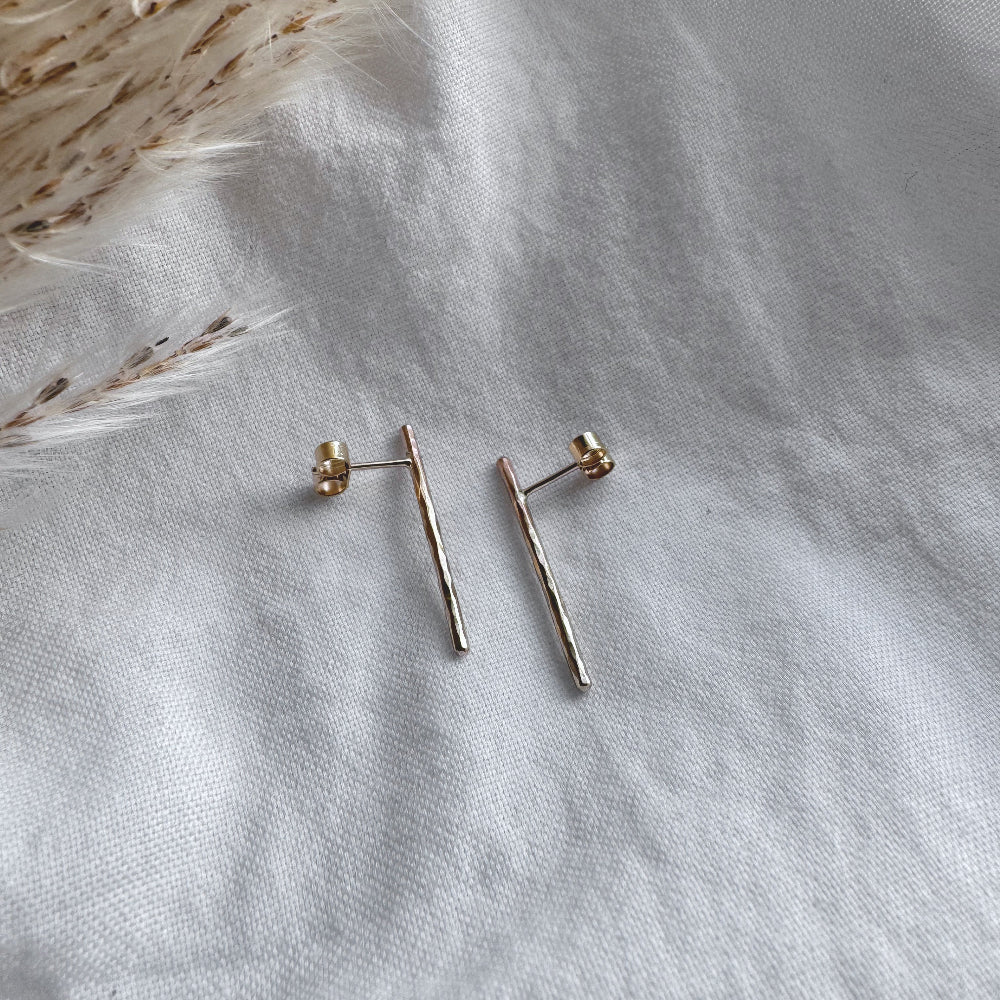 A pair of hammered gold bar earrings placed on a white fabric surface.