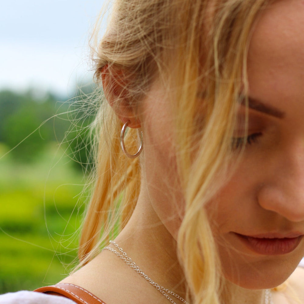 A lady with blonde hair wearing silver hoop earring with a green blurred garden in the background