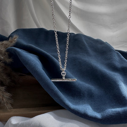 Silver necklace with a plain pendant on a blue fabric background