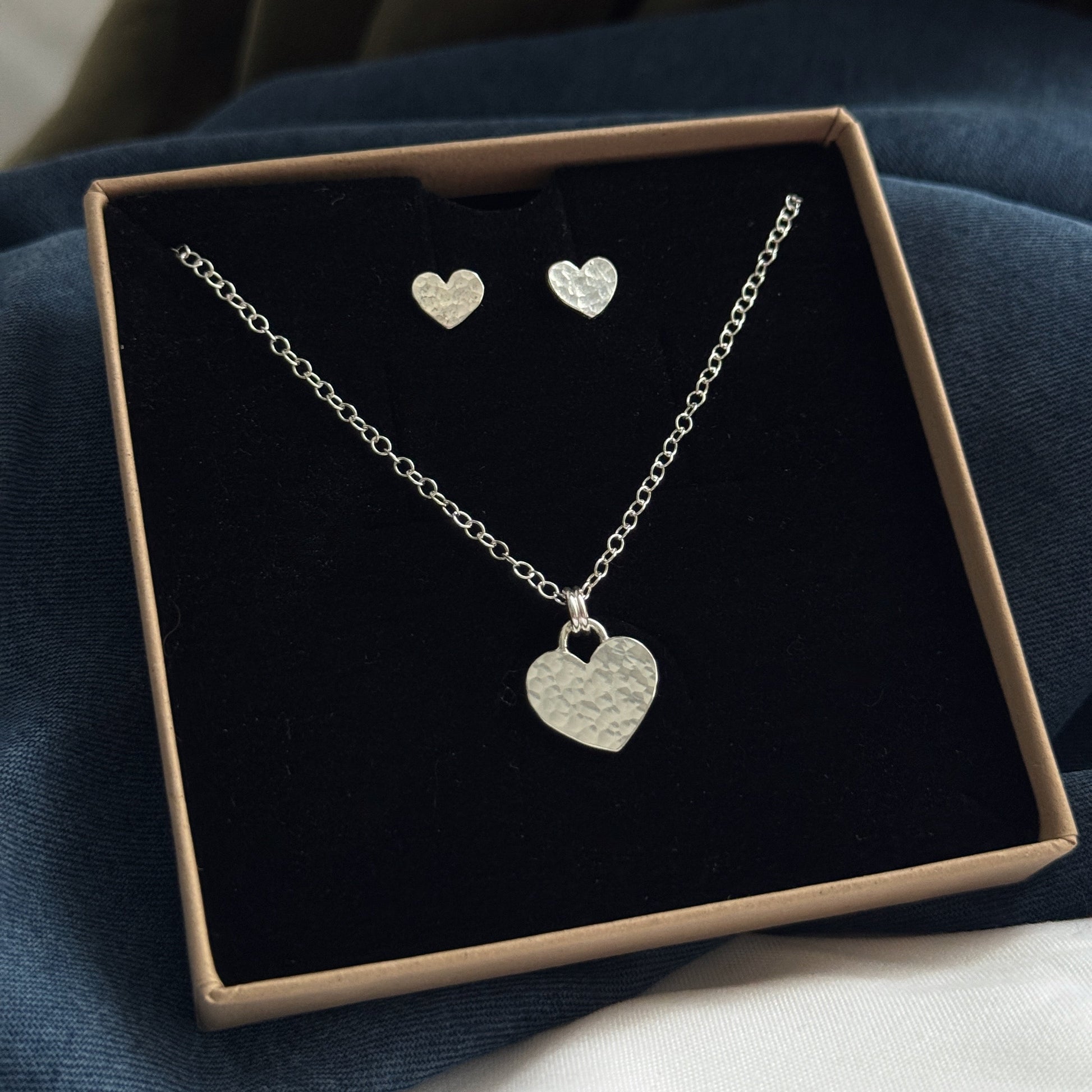 Silver heart necklace and earrings set in a box on a dark surface