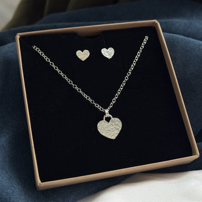 Silver heart necklace and earrings set in a box on a dark surface
