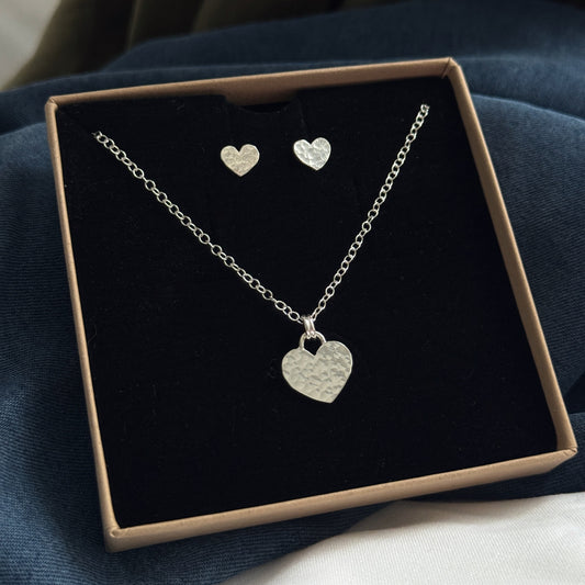 Silver heart necklace and earrings set in a box on a dark surface