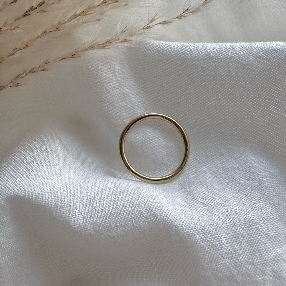 a simple gold plain band ring on a white fabric background