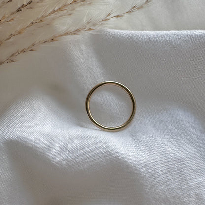 a simple gold plain band ring on a white fabric background