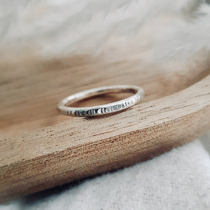 A silver infinity ring with hammered lines placed on a wooden surface.