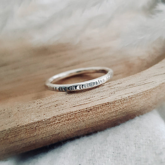 A silver infinity ring with hammered lines placed on a wooden surface.