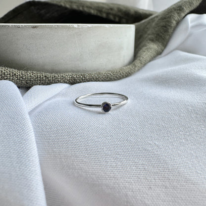 A silver ring with a blue/purple Iolite stone, placed on a white fabric surface.