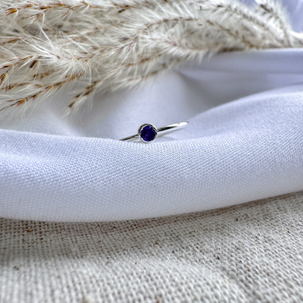 A silver ring with a blue/purple Iolite stone, placed on a white fabric surface.