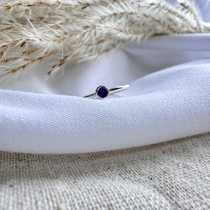 A silver ring with a blue/purple Iolite stone, placed on a white fabric surface.
