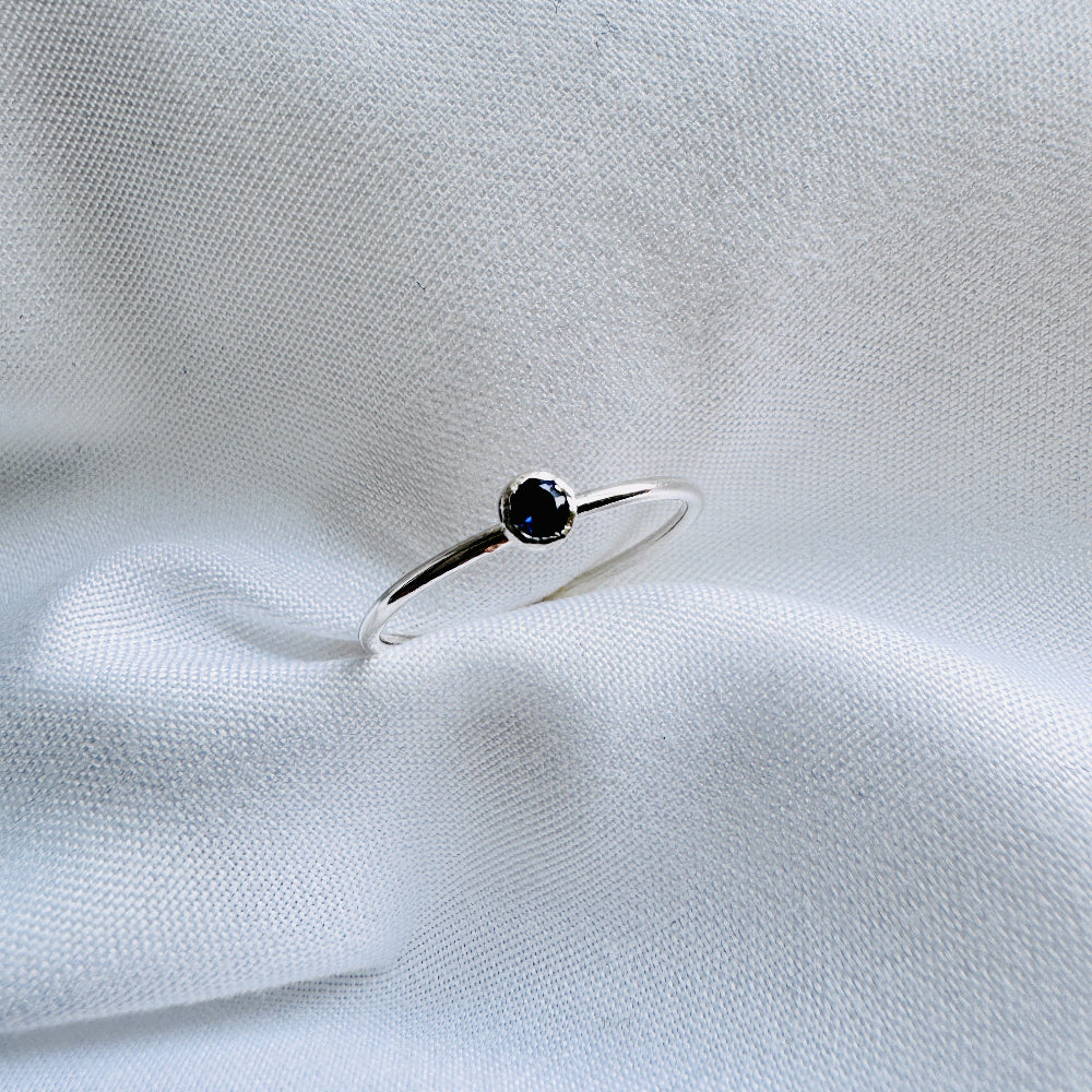 A silver ring with a blue/purple Iolite stone, placed on a white fabric surface.