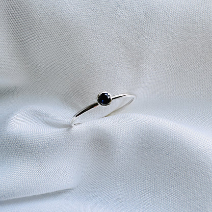 A silver ring with a blue/purple Iolite stone, placed on a white fabric surface.