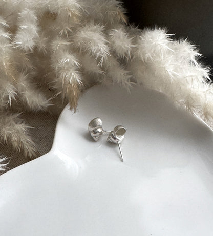 Silver periwinkle shell stud earrings on a white surface with dried white  fluffly grass in the background