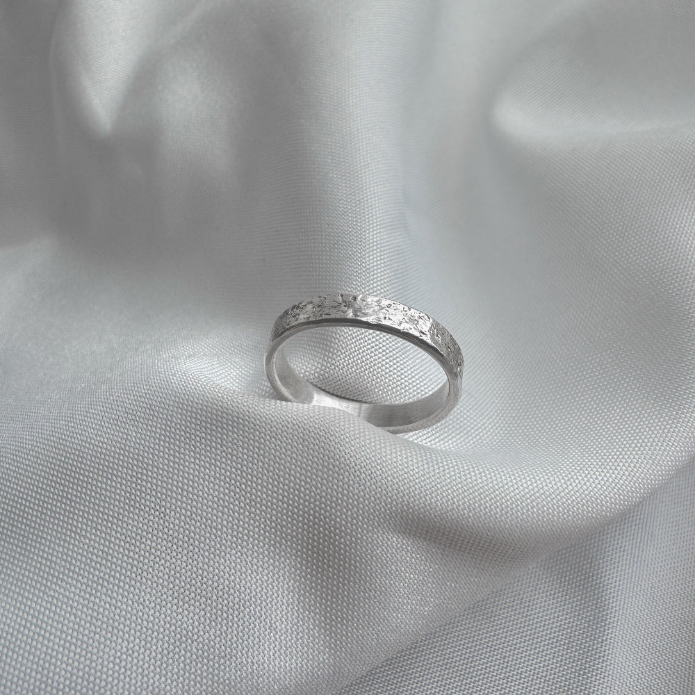 Silver ring with sand texture on a light gray fabric background